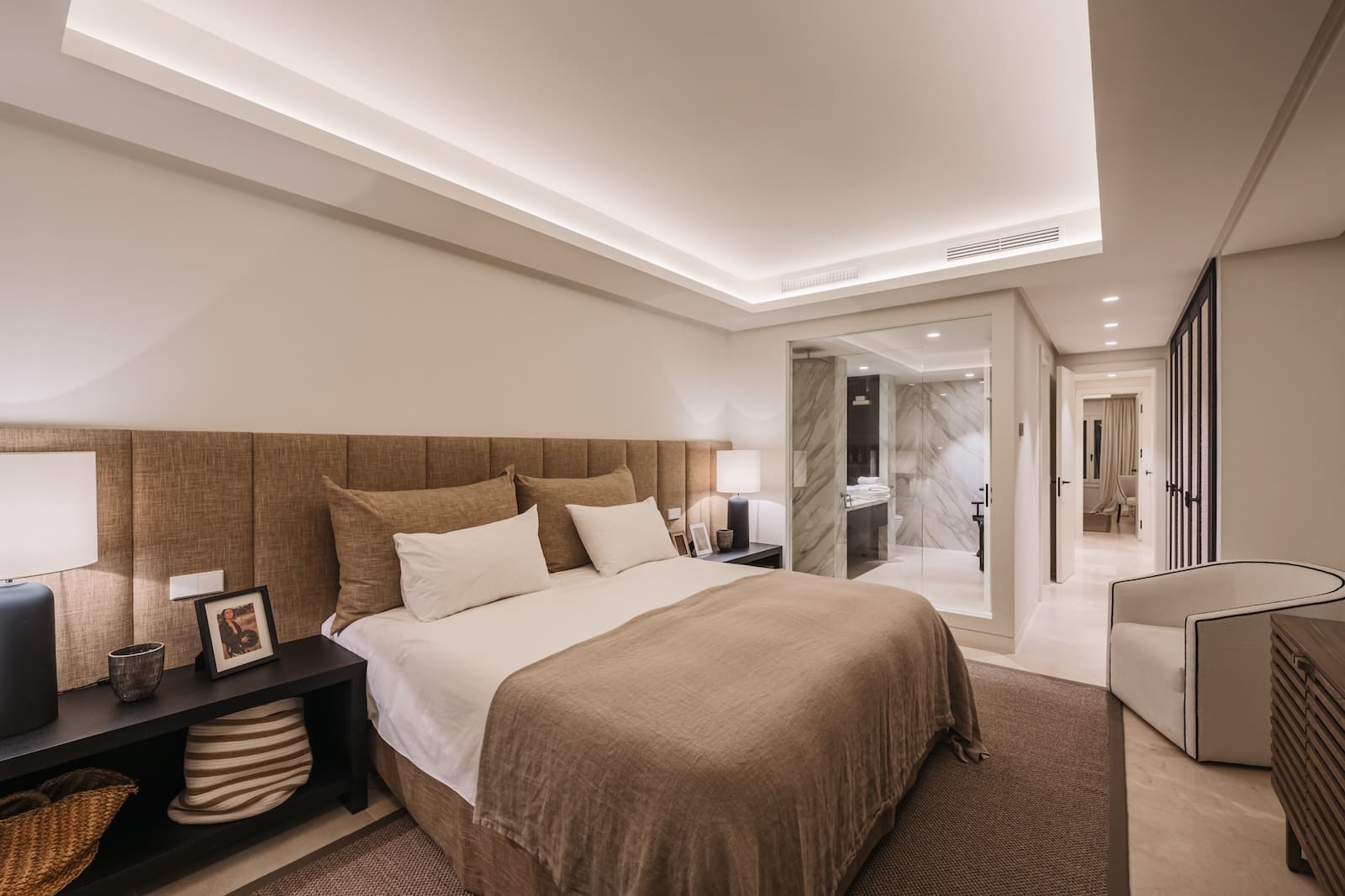 Luxurious hotel bedroom with a king bed, beige headboard, and matching linens; nightstands and lamps on both sides.