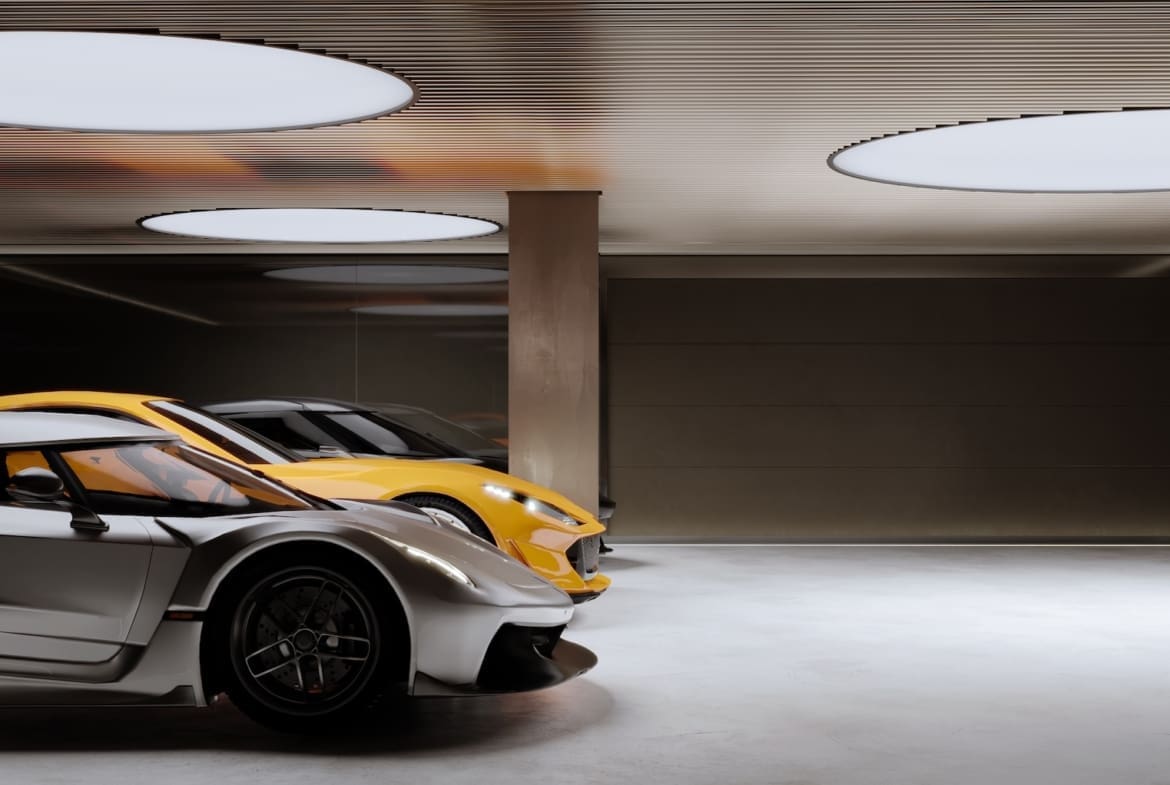 Two sports cars—silver and yellow—parked in a modern underground garage with round ceiling lights and a concrete column nearby.