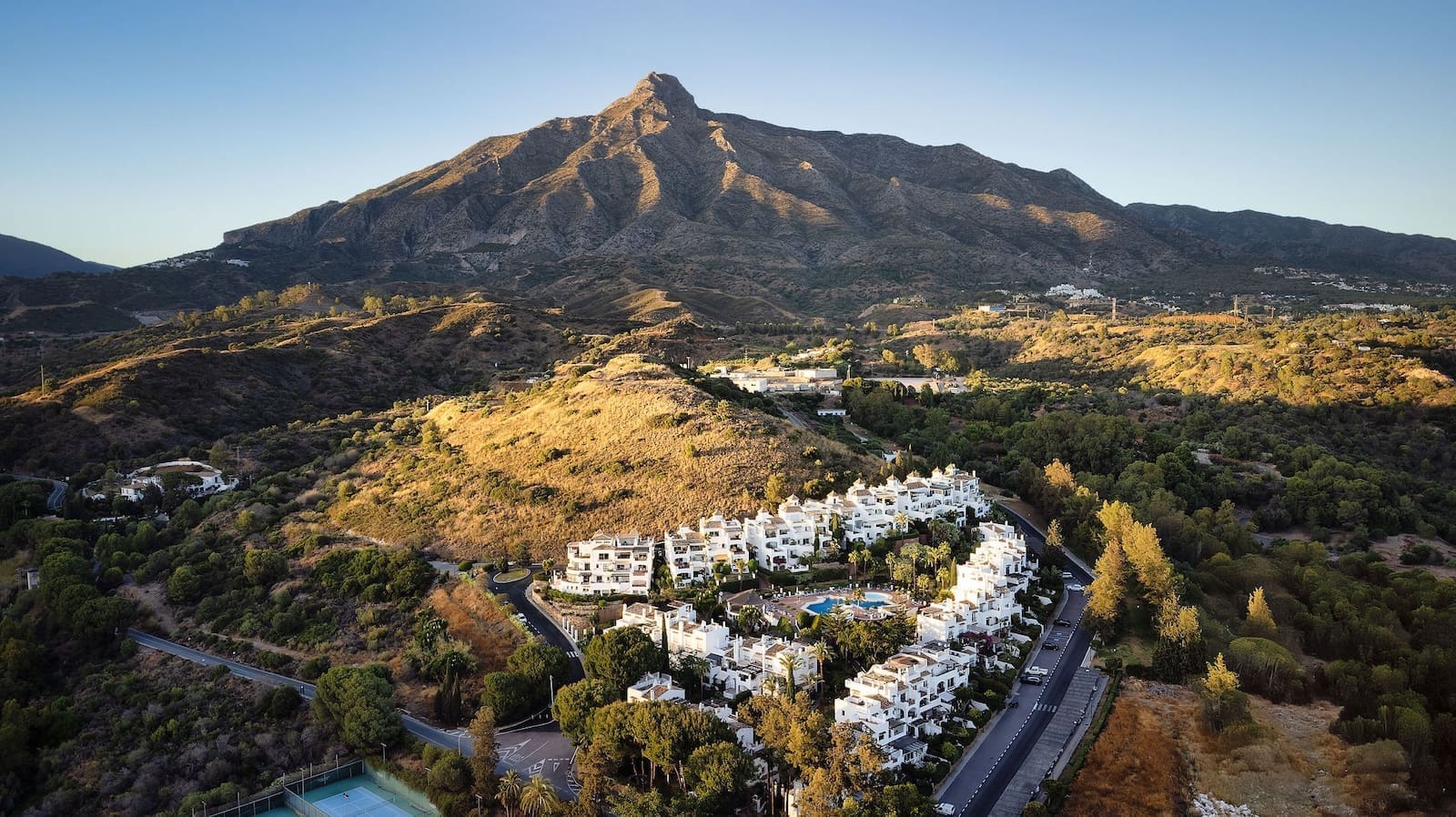 La Maison Saint Germain luxury townhouse Golden Mile Marbella – MDR Luxury Homes 43 Aerial view of white apartment buildings clustered on a hillside with a mountain in the background and a pool center.