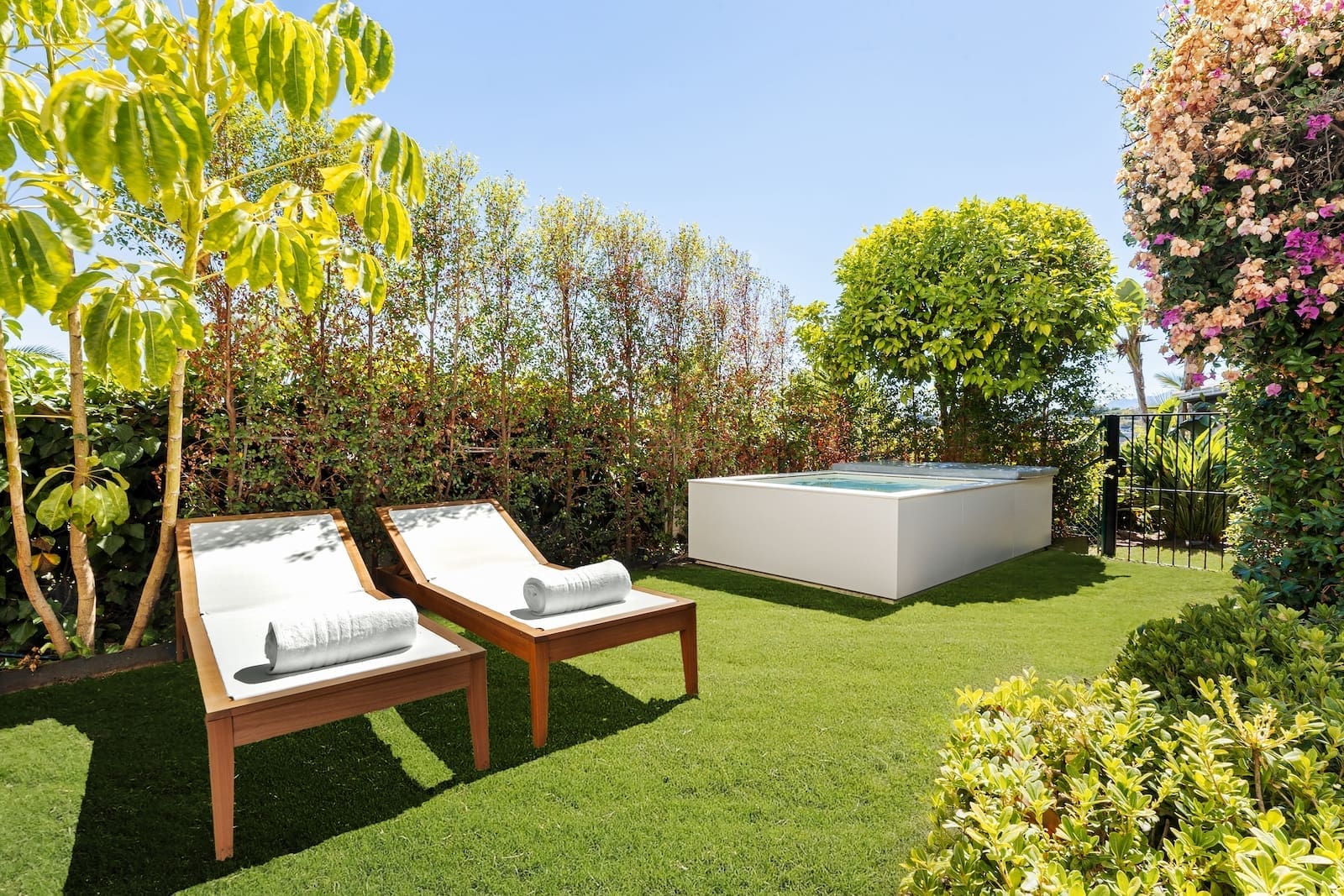La Maison Saint Germain luxury townhouse Golden Mile Marbella – MDR Luxury Homes 47 Two wooden sun loungers with white cushions and rolled towels on a green lawn in a sunny garden beside a raised rectangular pool.